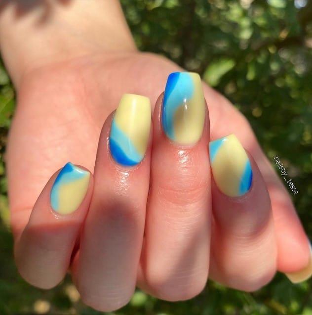 a woman with pale yellow nails with ocean blue and light teal swirls