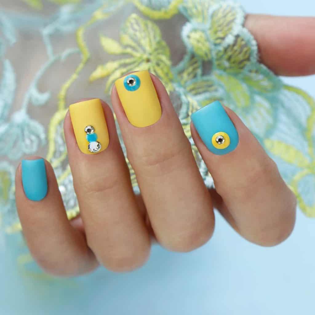 a woman with pale yellow and light blue nails with carefully placed rhinestone nail gems outlined with either blue or yellow