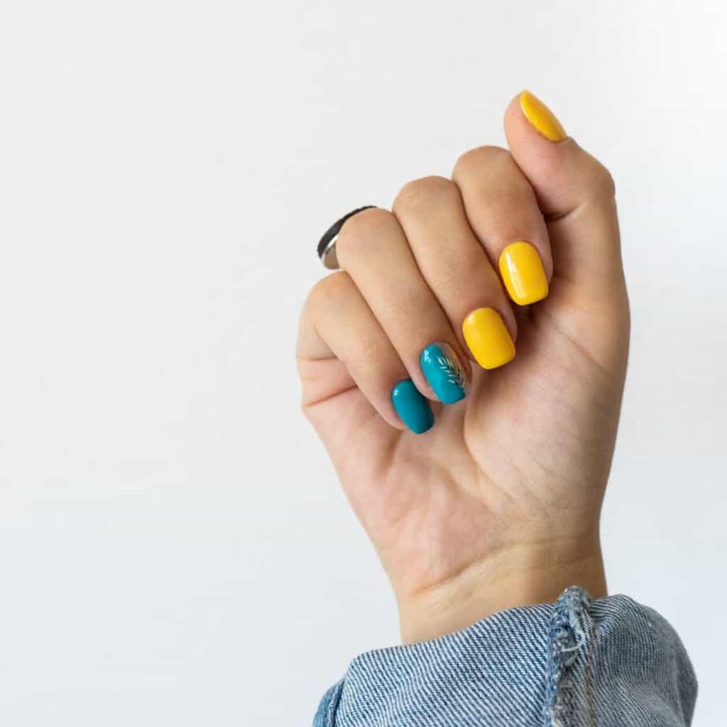 a woman with deeper hues like dark aqua and goldenrod for a distinctive take on yellow and blue nails