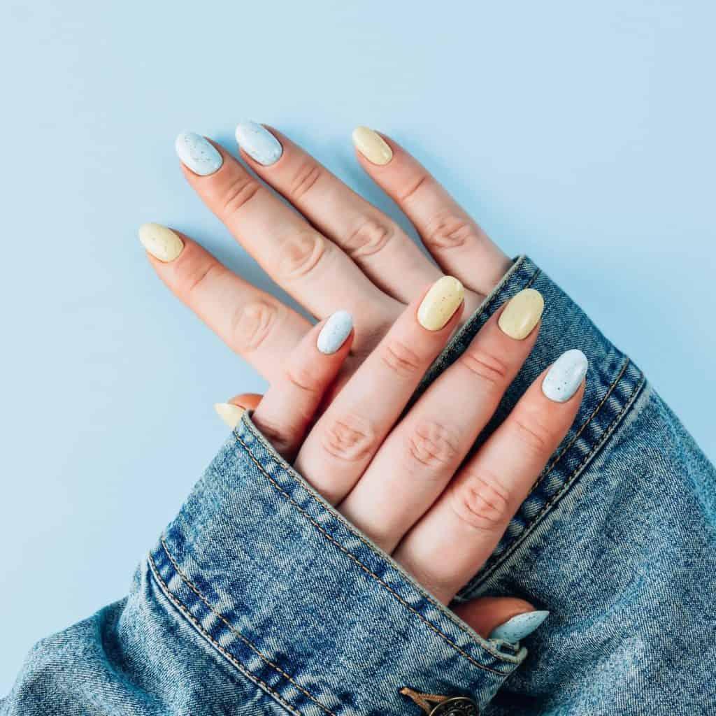 a woman wearing denim jacket with pale blue and yellow nail polish