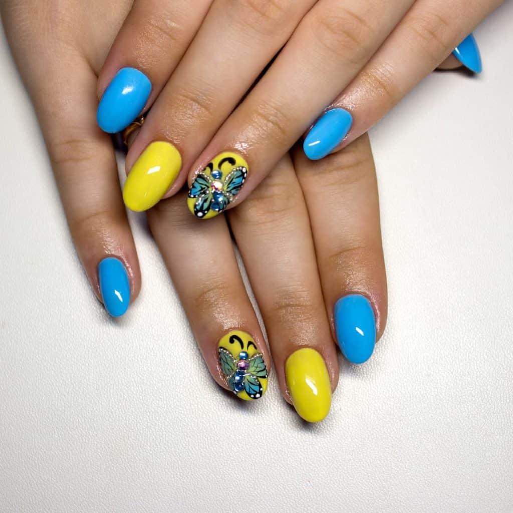 a woman with blue and yellow nails with butterfly design punctuated with nail gems
