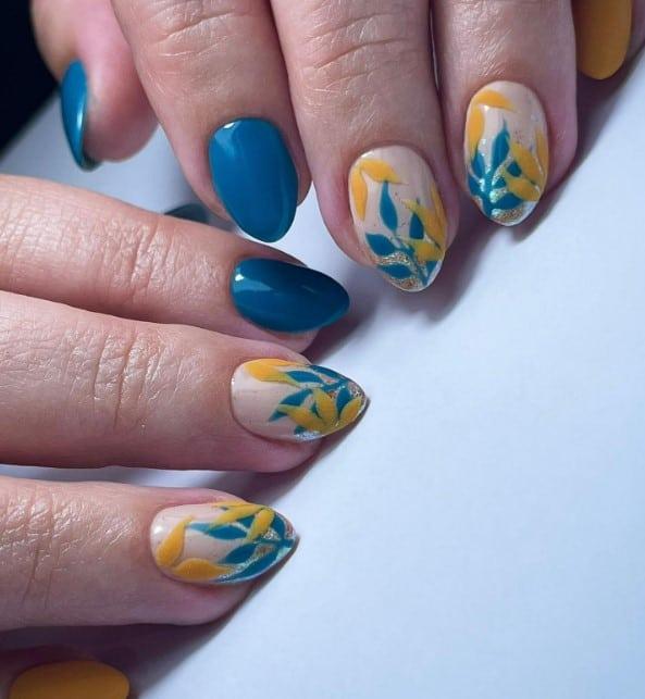 a woman's nails colored in deep teal and mustard yellow with floral and gold designs