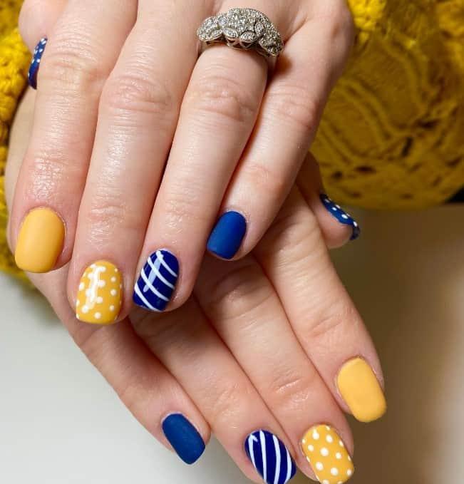 a woman's nails in dark blue and yellow hue with white stripes as accent