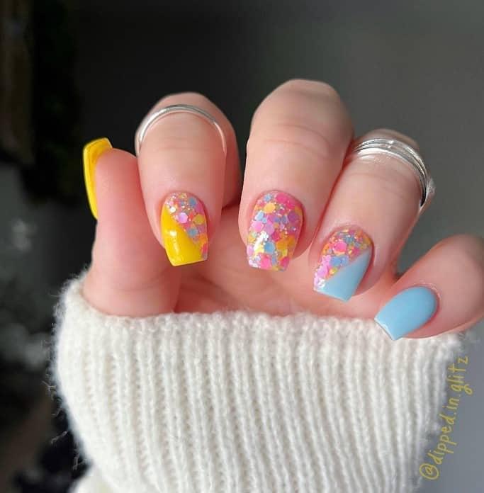 a woman's hand painted in blue and yellow with chunky, confetti-like, and multicolored glitter flakes