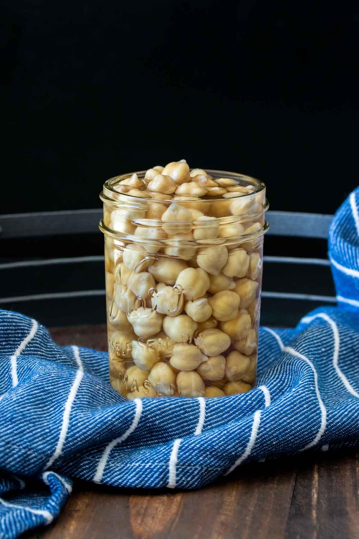 Glass jar filled with water and dried chickpeas filled up halfway inside.