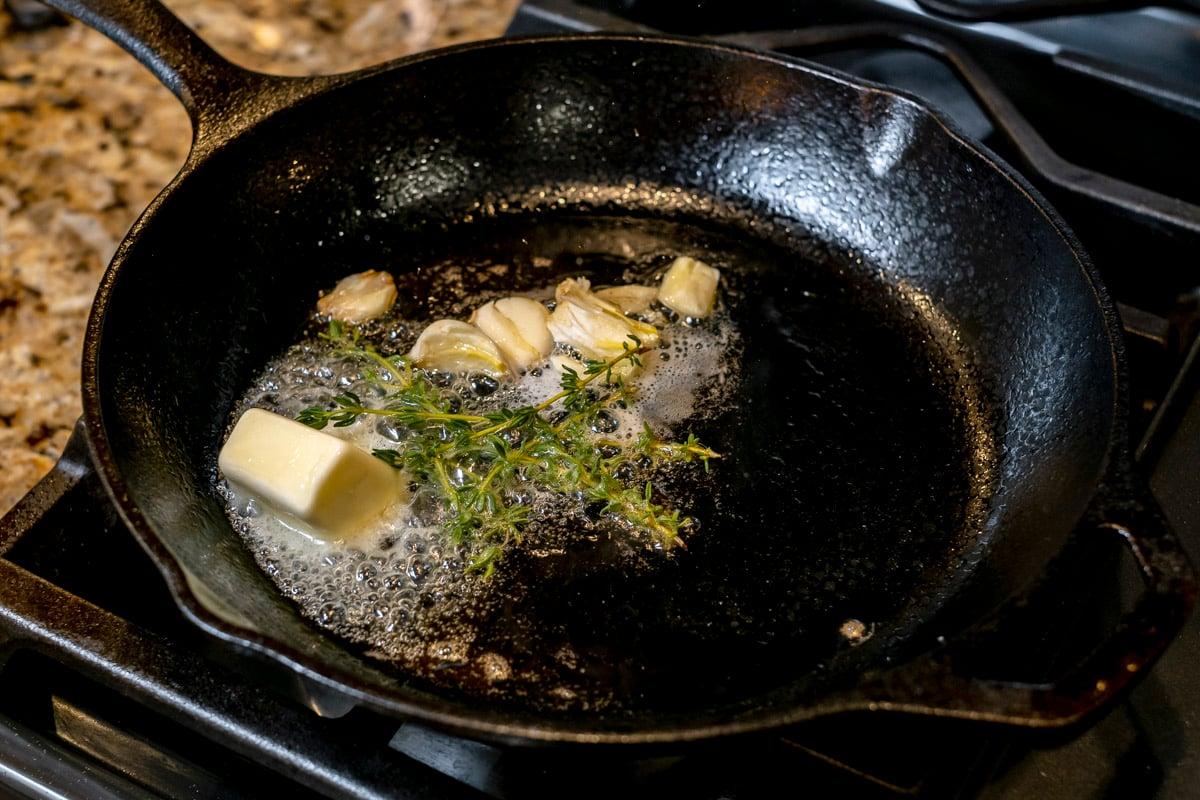 butter melting with garlic and thyme in cast iron pan.