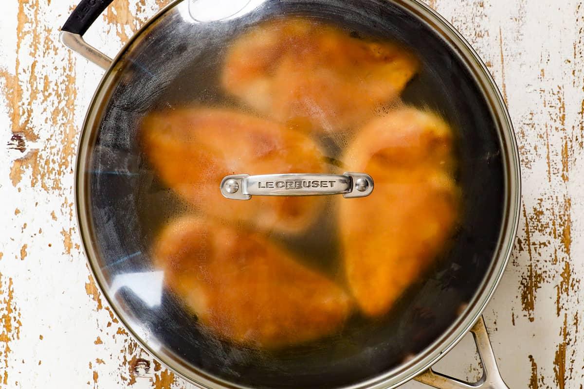 showing how to make shredded chicken by adding chicken broth to the chicken in a pan, covering, and steaming