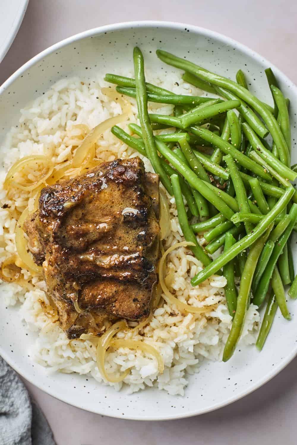 Roasted pork neck bones over rice next to green beans on a plate.