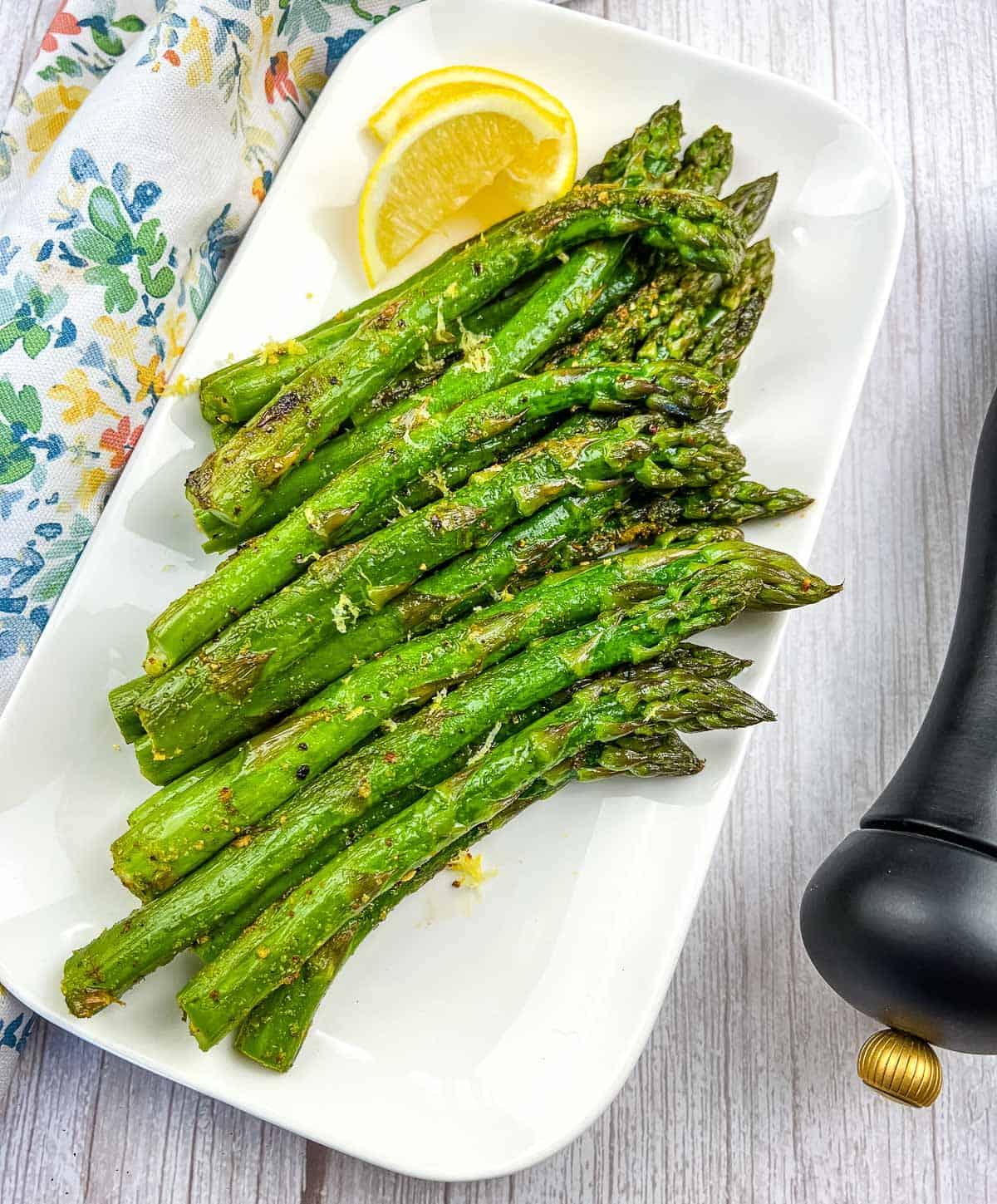 griddled asparagus on a white platter with lemon wedges