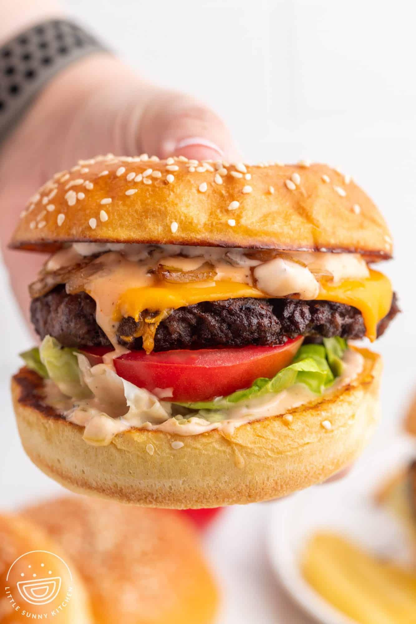 A hand holding a juicy stovetop burger with all the toppings.
