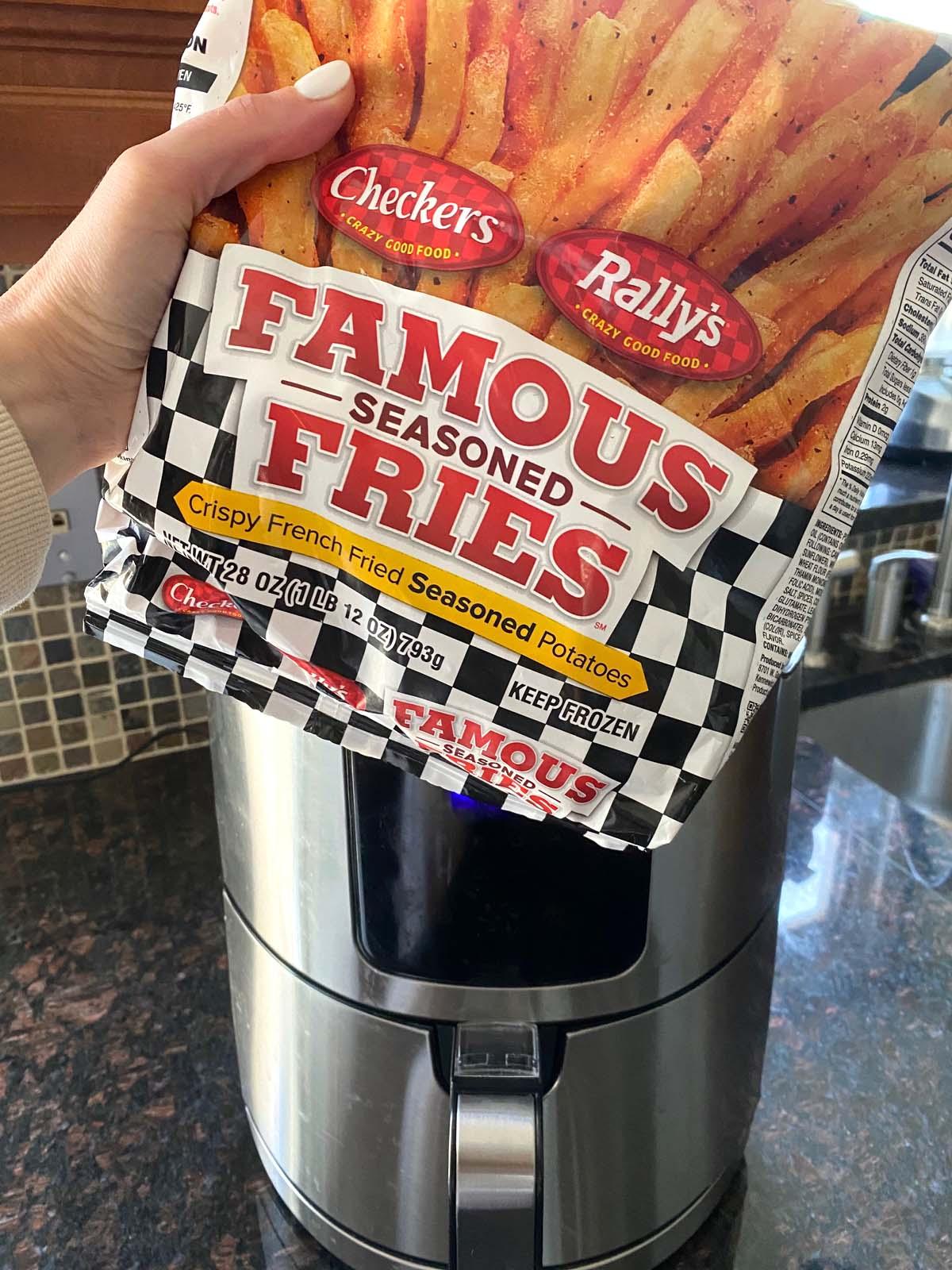 A bag of frozen Checkers famous seasoned fries being held in front of an air fryer.