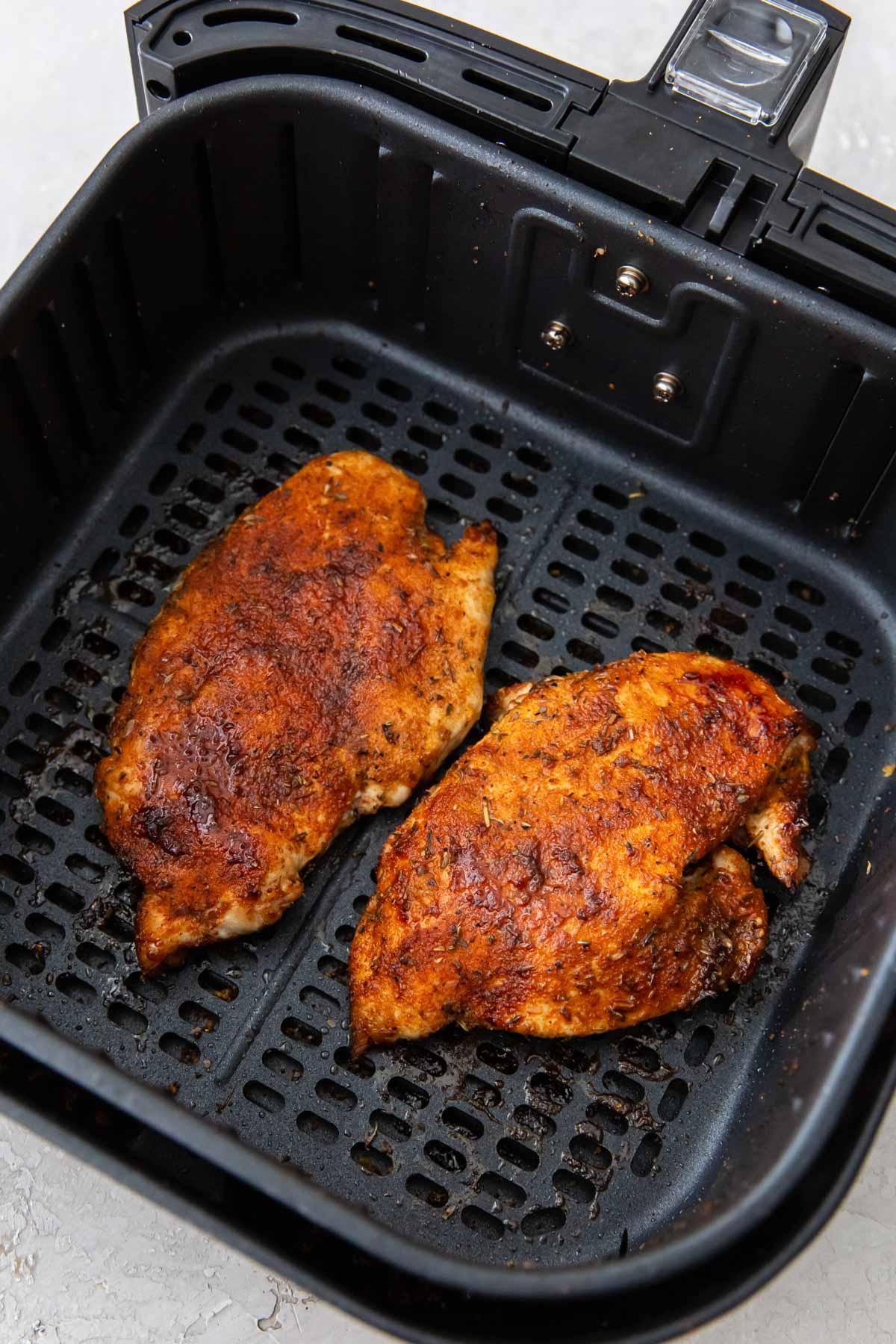 Two cooked chicken breasts in an air fryer