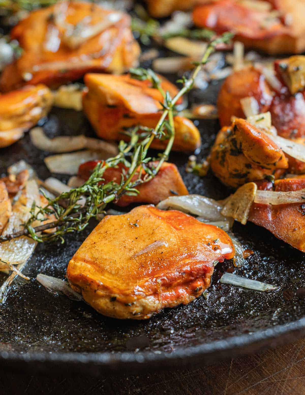 A close up image of chicken of the woods mushrooms cooking in a pan with shallots, garlic, and thyme sprigs
