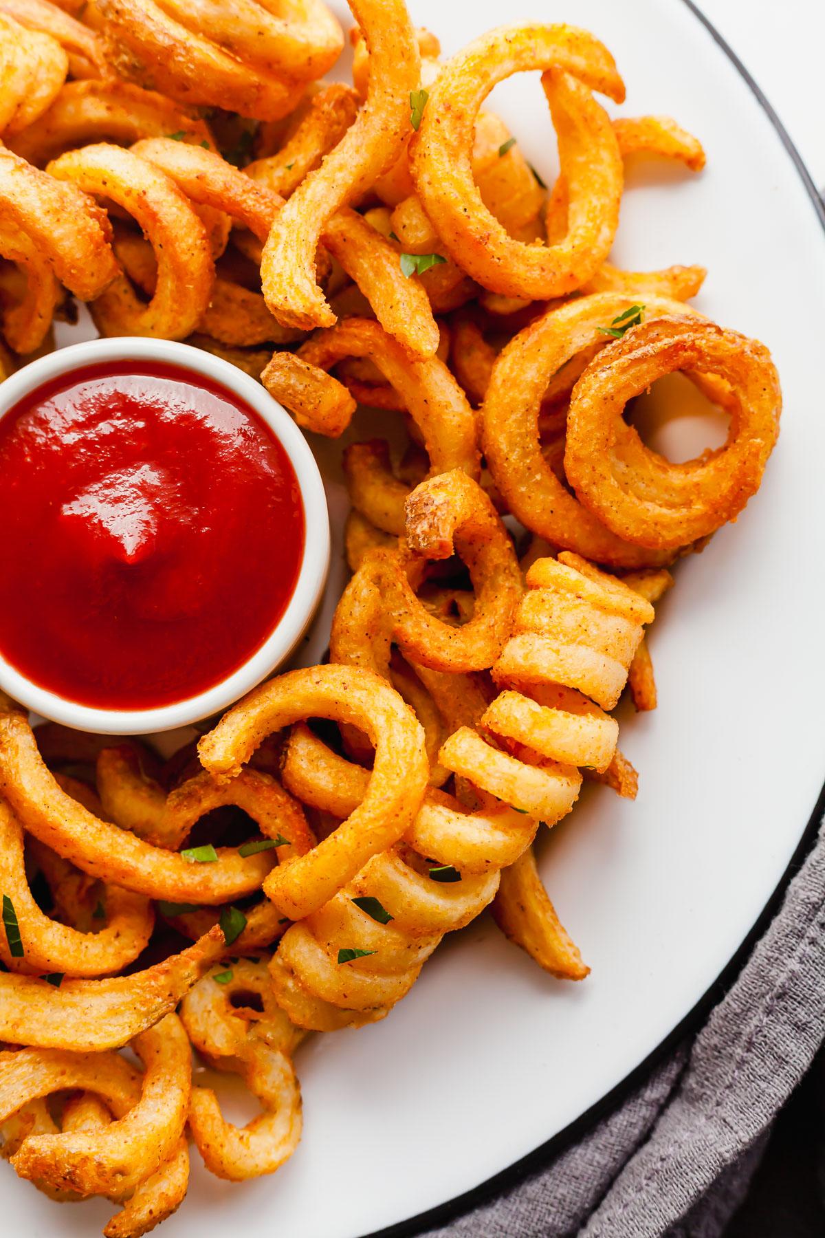 hand dipping a curly fry into a container of ketchup