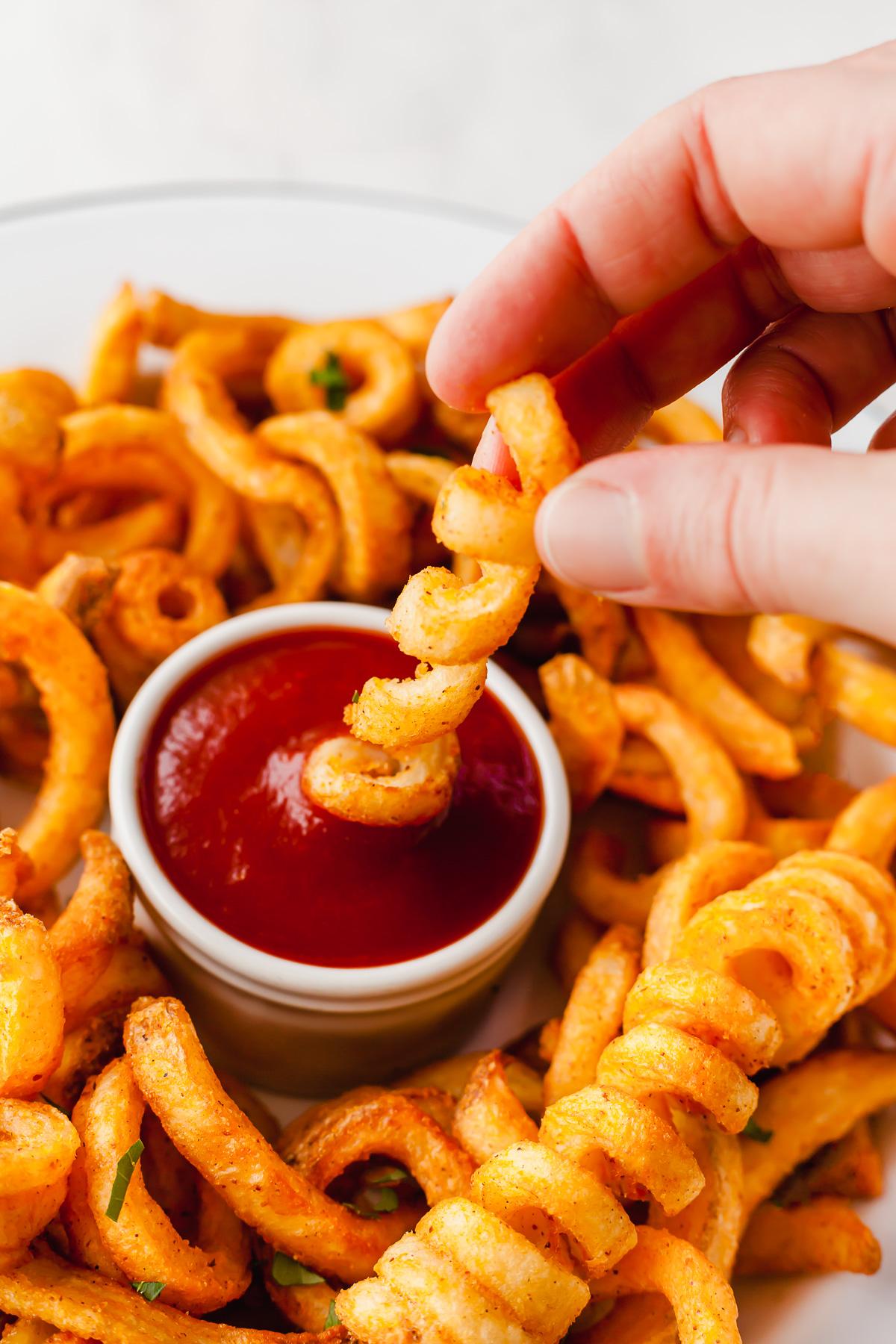a close-up of frozen curly fries made in the air fryer on a plate surrounding a bowl of ketchup