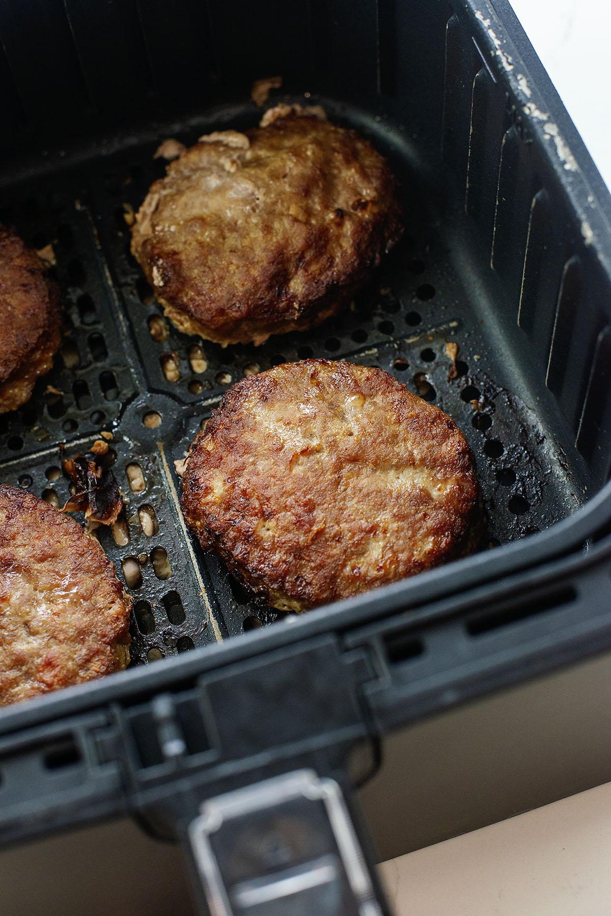 Cooked turkey burgers in an air fryer basket.