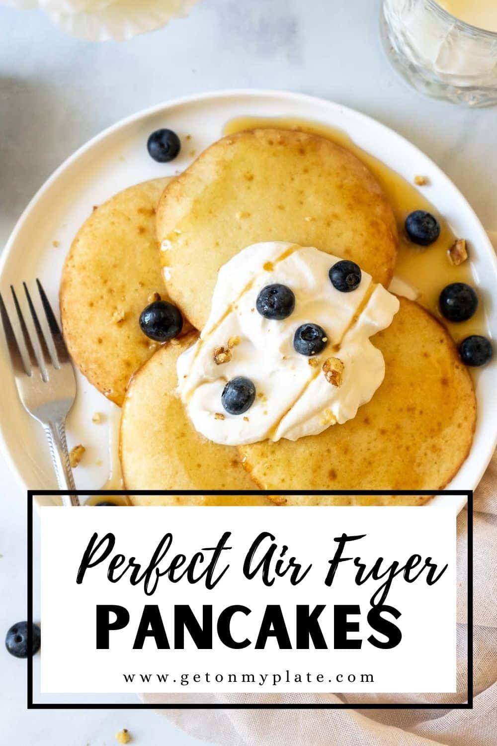 Four air fryer pancakes on a plate with whipped cream, blueberries, and maple syrup.