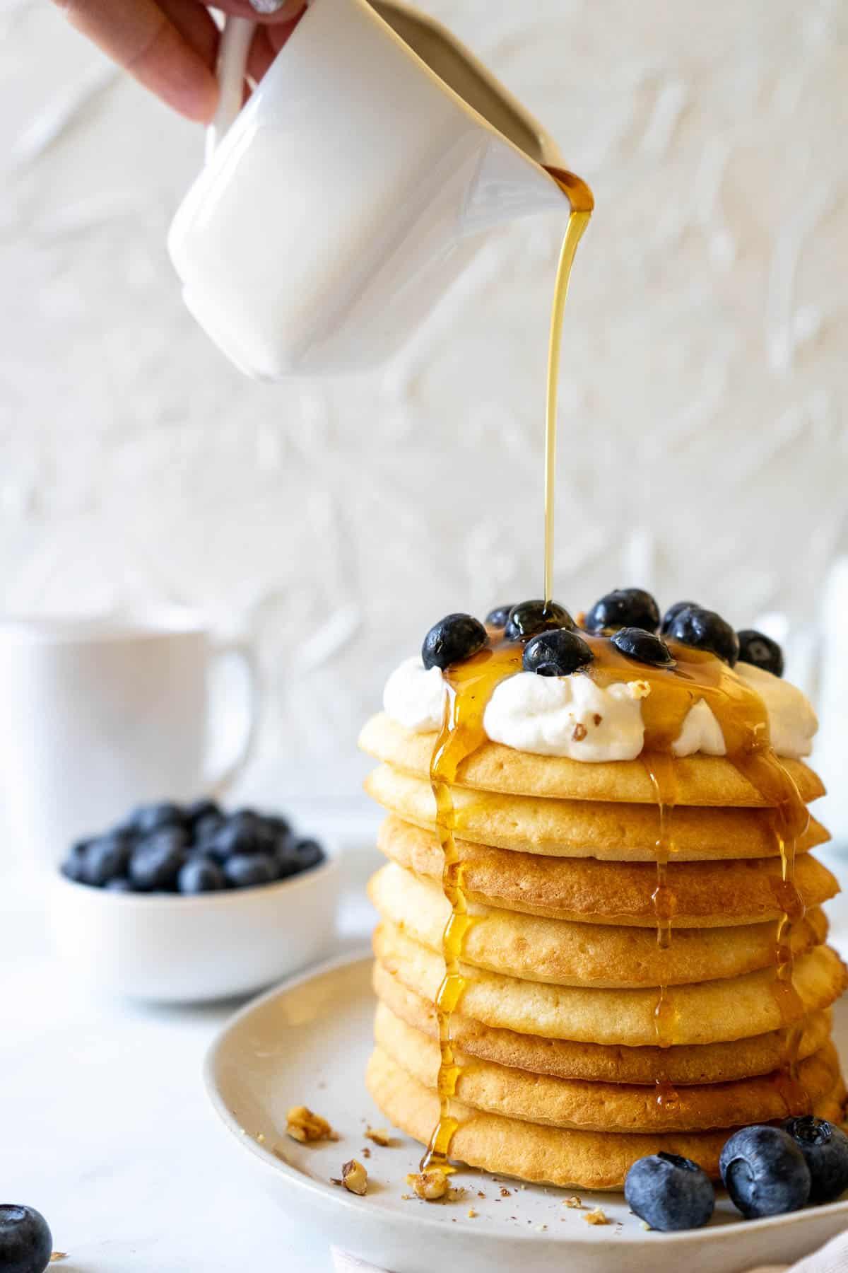 Four air fryer pancakes on a plate with whipped cream, blueberries, and maple syrup.