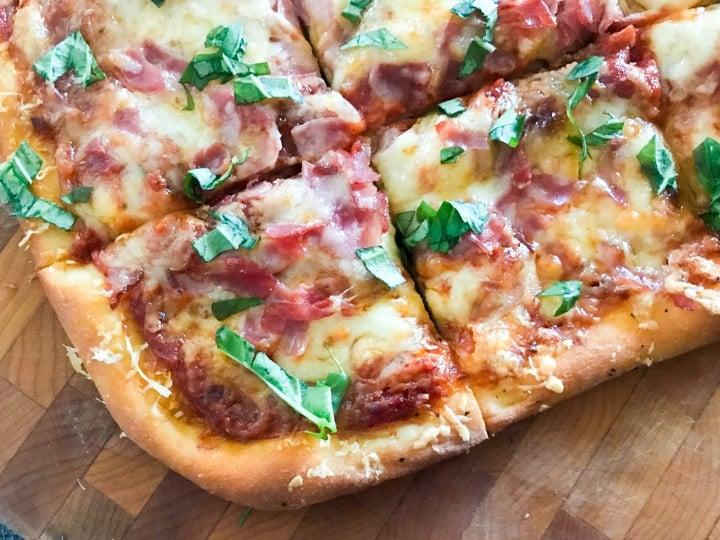 homemade pizza topped with cheese ham and fresh basil