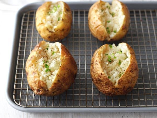 Golden baked potatoes on a rack inside a cooking pan.