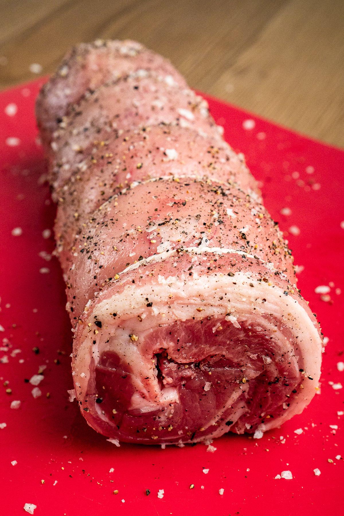 Lamb Breast Joint seasoned with salt and pepper on a red chopping board