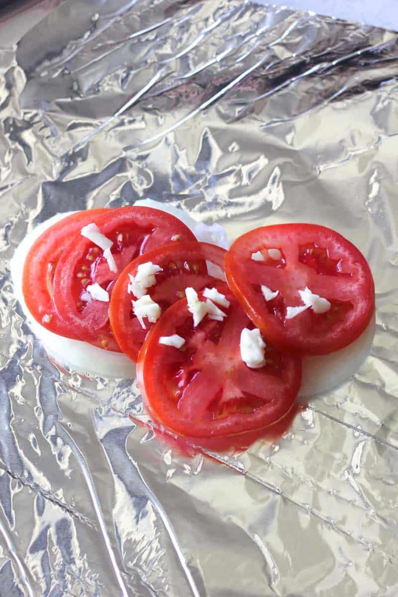 Sliced onions and tomatoes with chopped garlic on the foil
