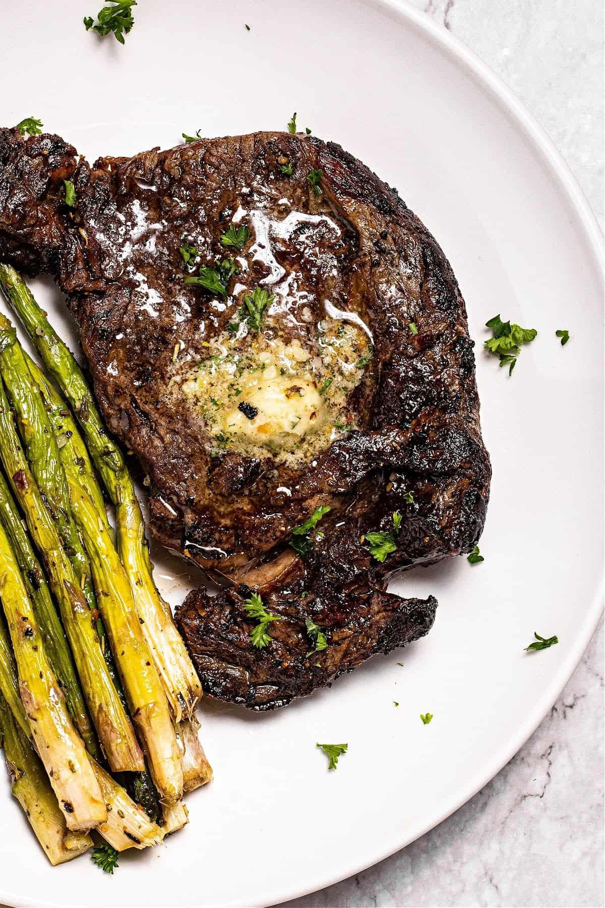 ninja air fryer steak topped with compound garlic butter on a plate with air fryer asparagus