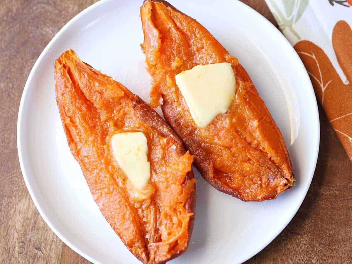 Two microwave sweet potato halves served on a white plate and topped with butter.