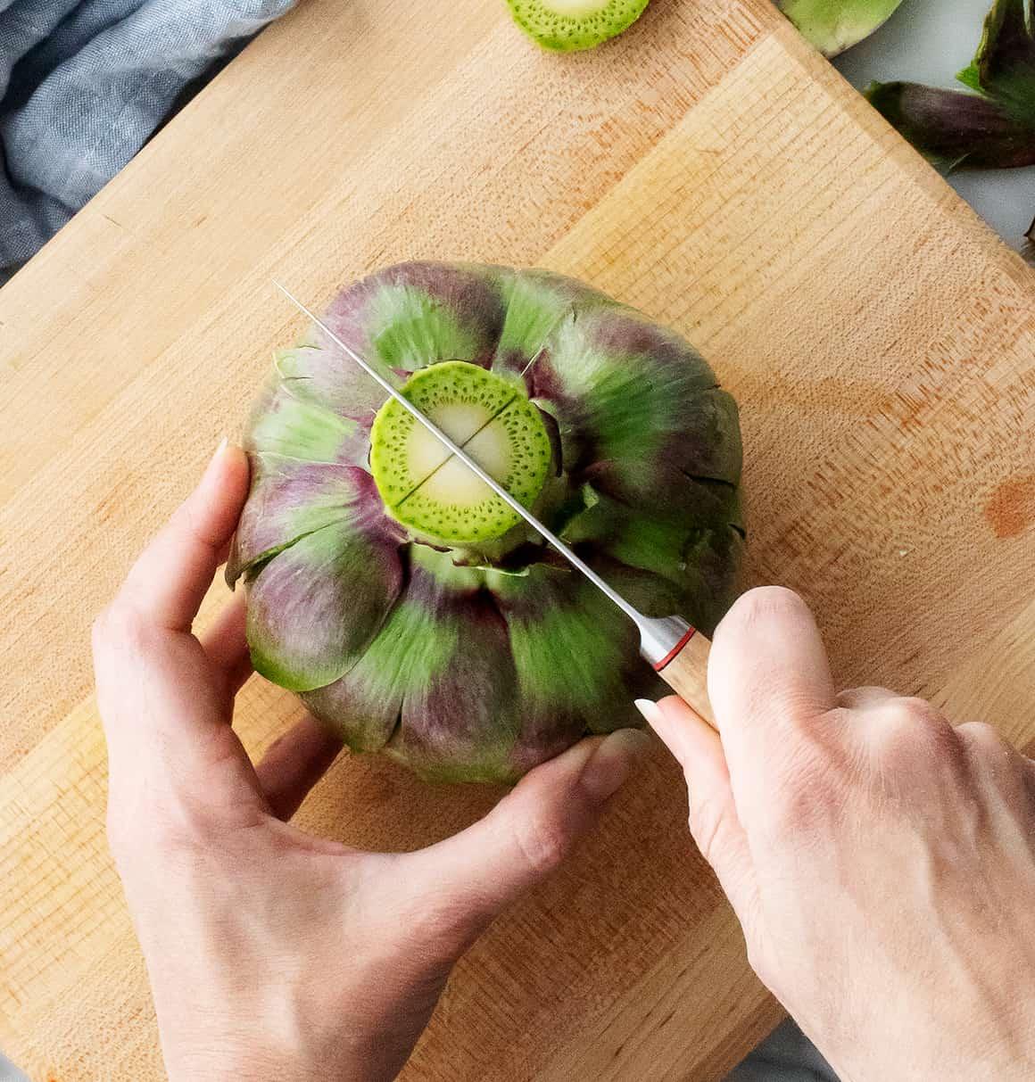 Hands scoring artichoke stem with a knife