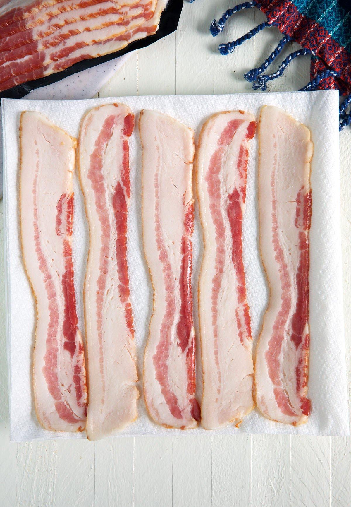 Raw bacon is placed on a sheet of paper towels.