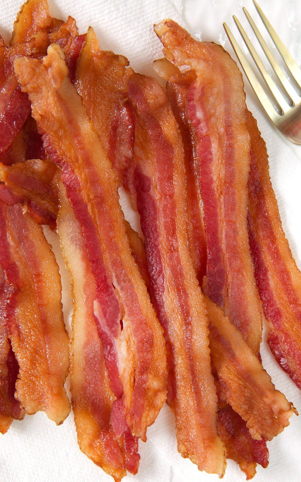 A stack of cooked bacon is placed on a paper towel.