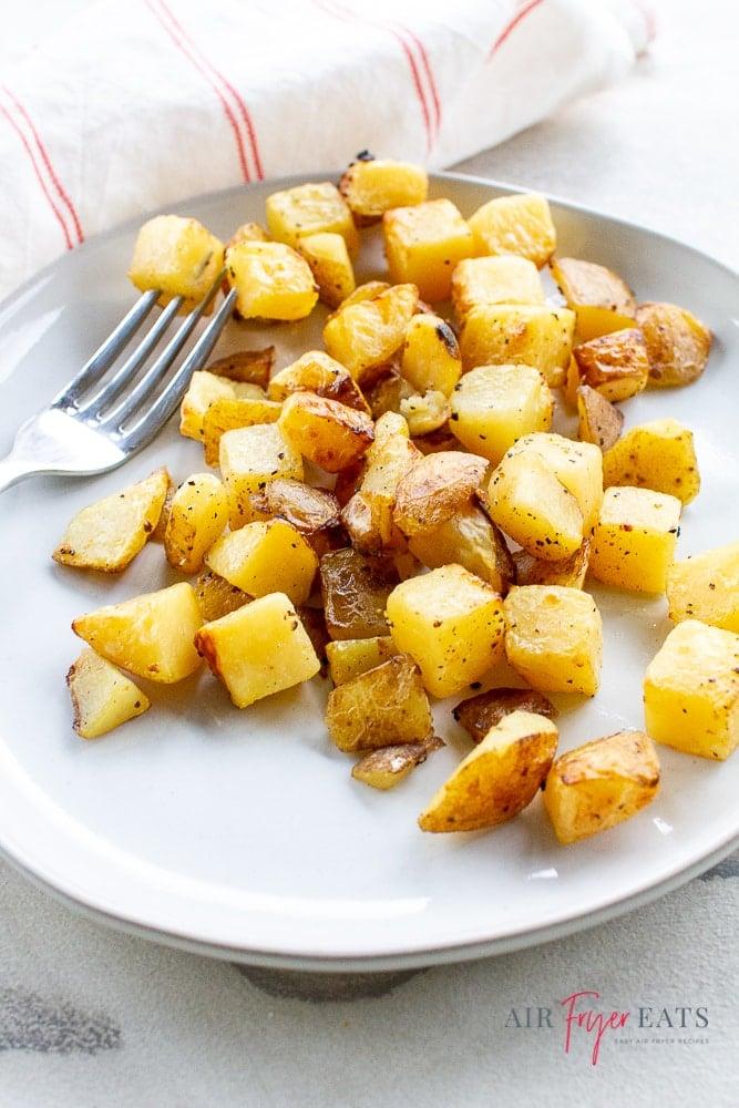 Crispy golden brown air fried potatoes on a white plate with a fork