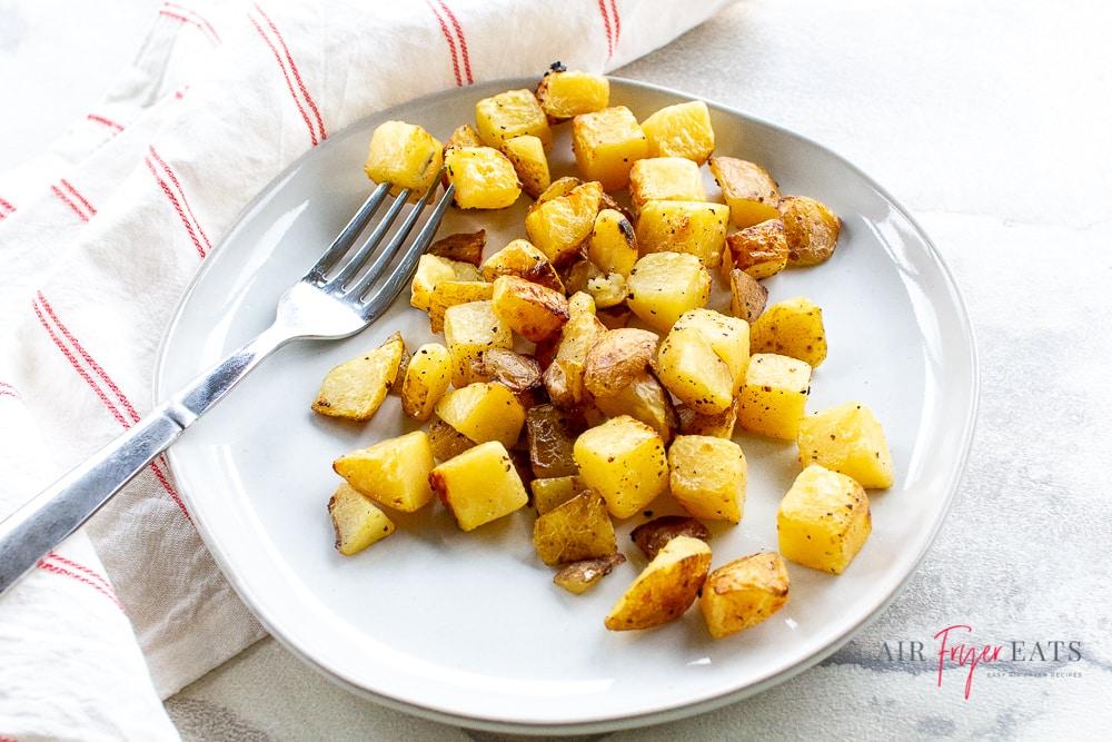 Landscape style photograph of white plate with golden brown potato cubes and a silver fork