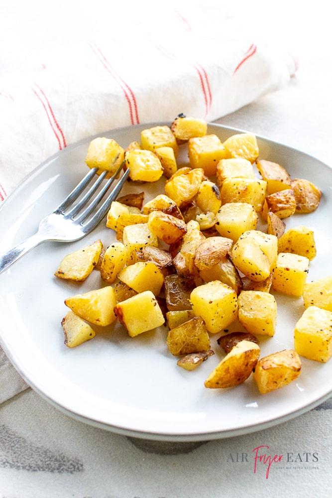 Vertical shot of golden brown seasoned potatoes on a plate with white napkin and a fork