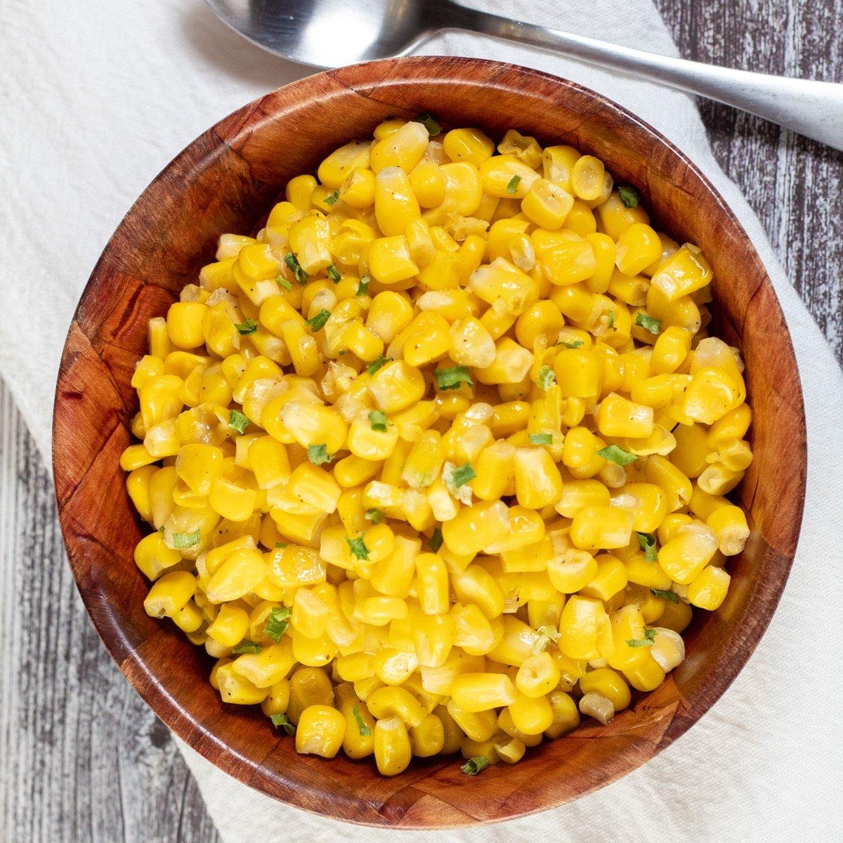 Square image showing cooked canned corn in a wooden bowl.