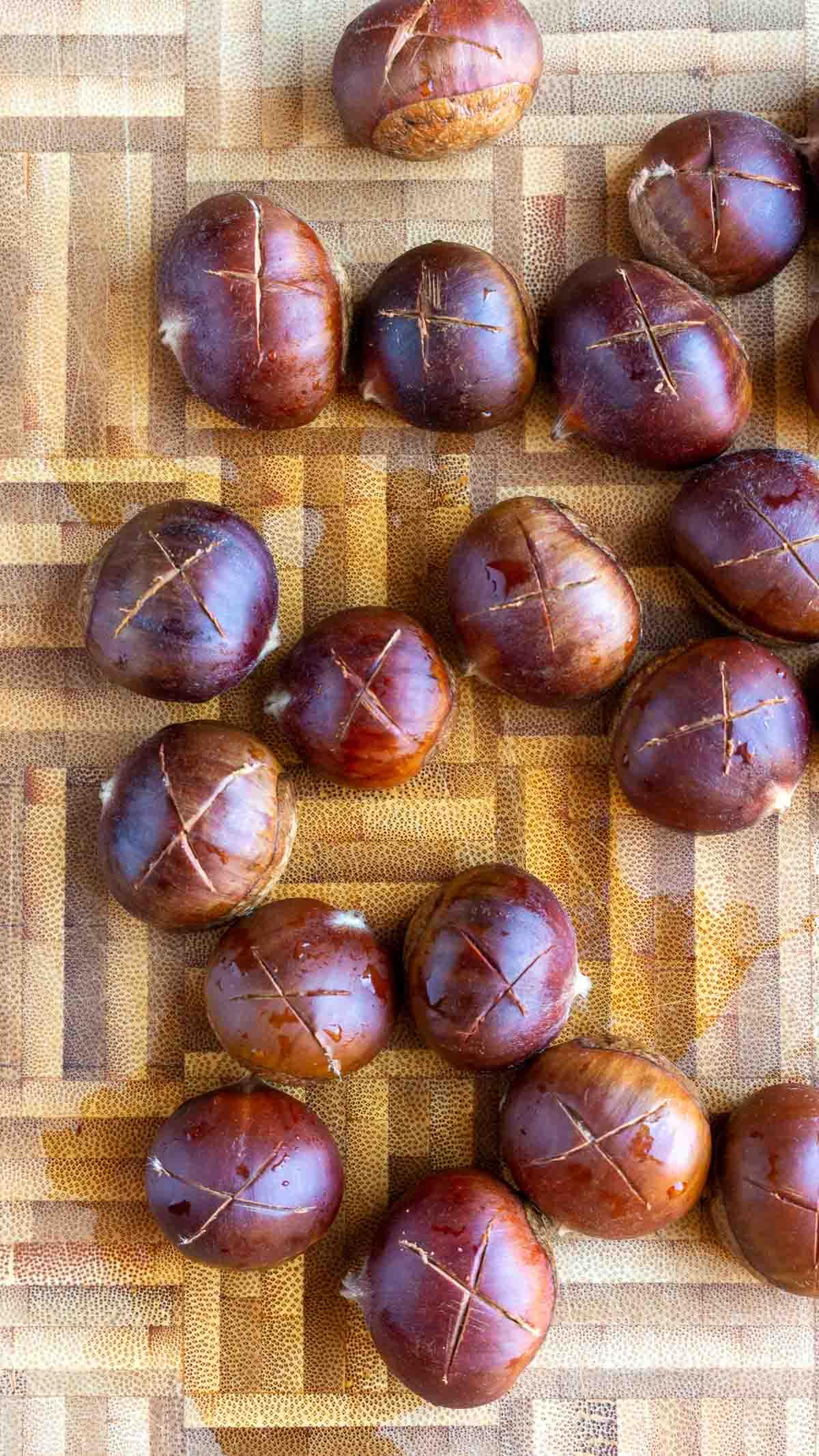 Raw chestnuts with a score of an "X" on a cutting board