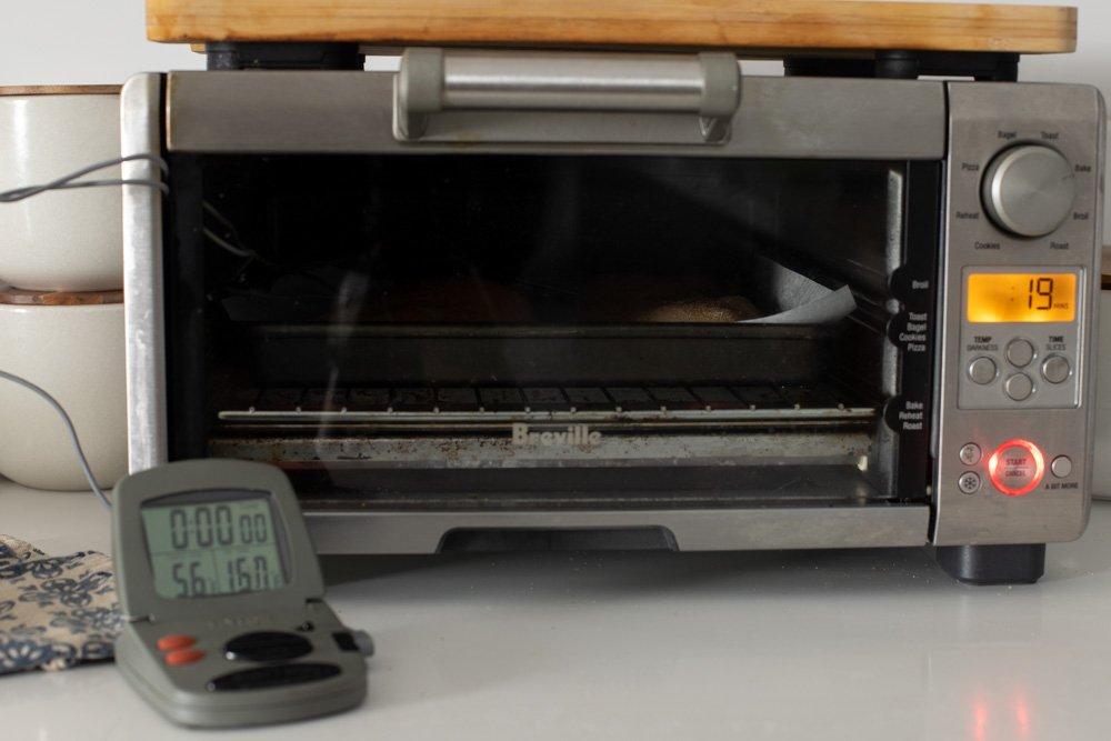 Toaster oven on counter with chicken baking. Meat thermometer in front left.