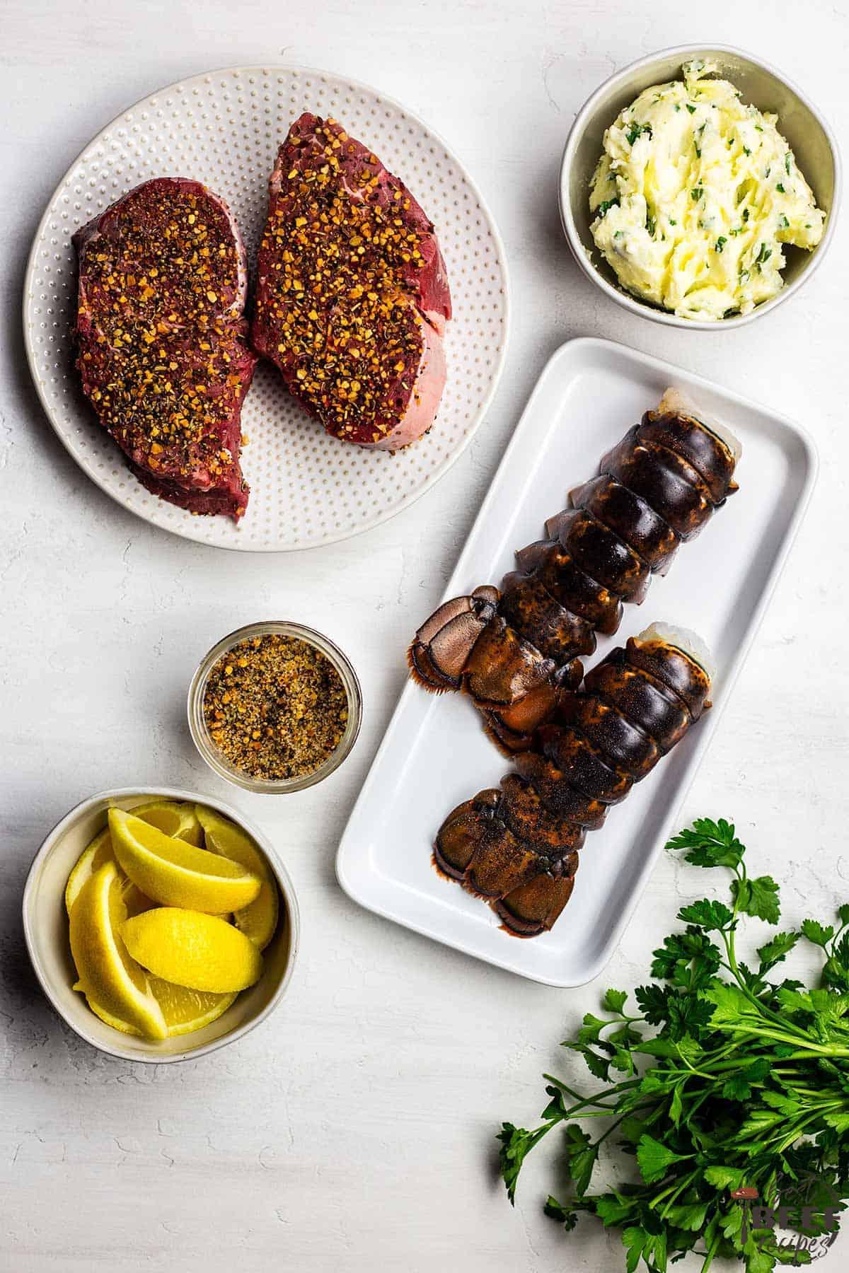 The ingredients to make air fried steak as well as lobster tails and garlic butter on a white surface, top-down view