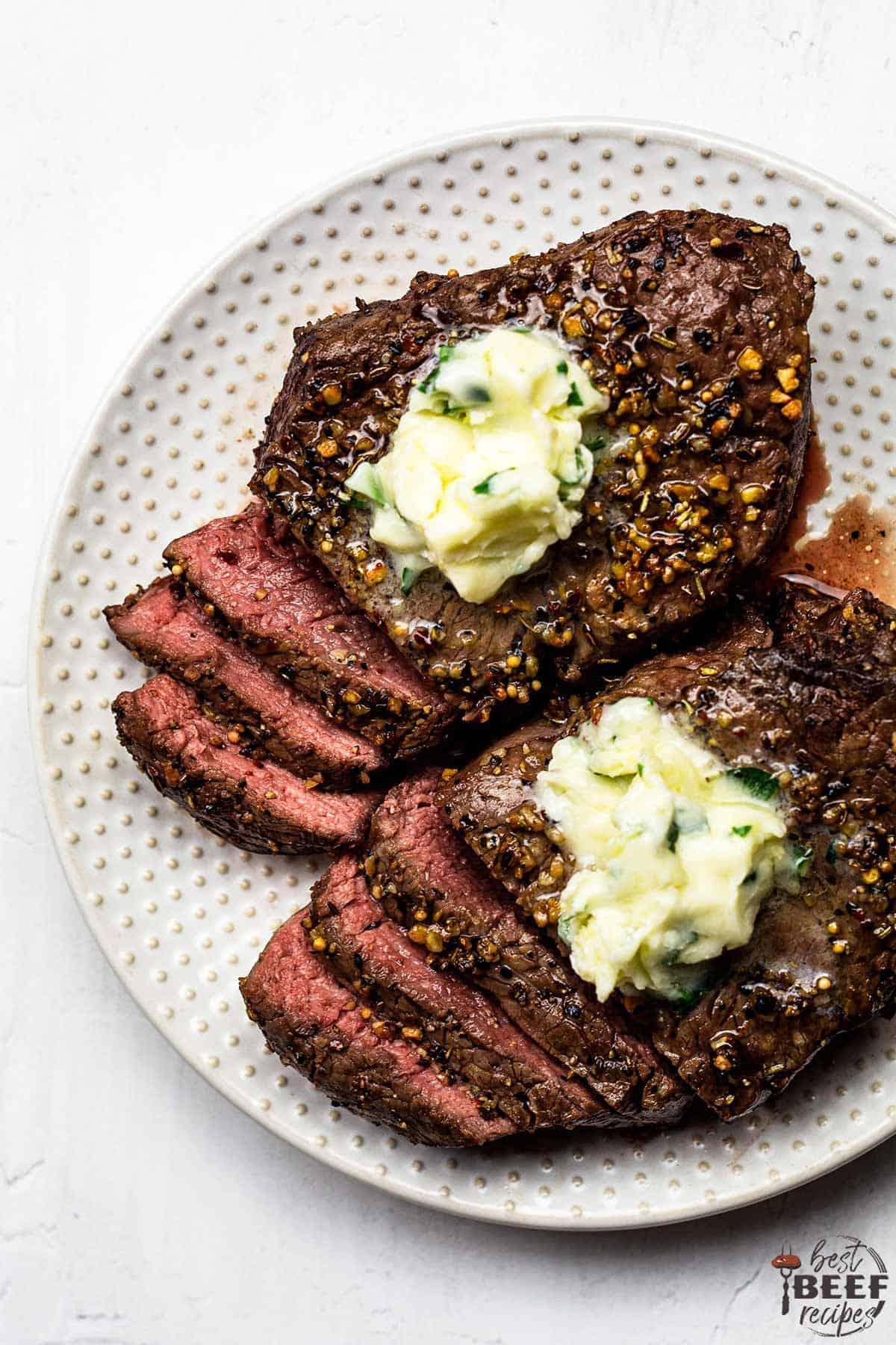 A plate of two air fryer steaks with garlic butter on top, partially cut into slices