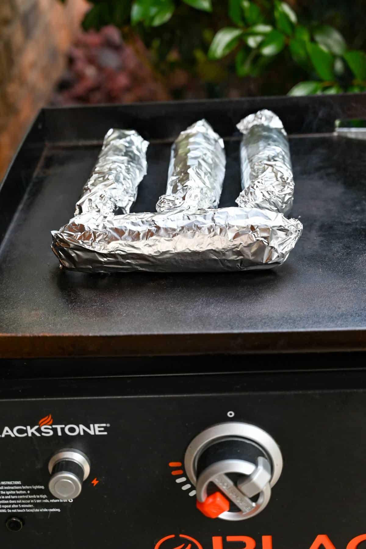 corn wrapped in foil cooking on a griddle