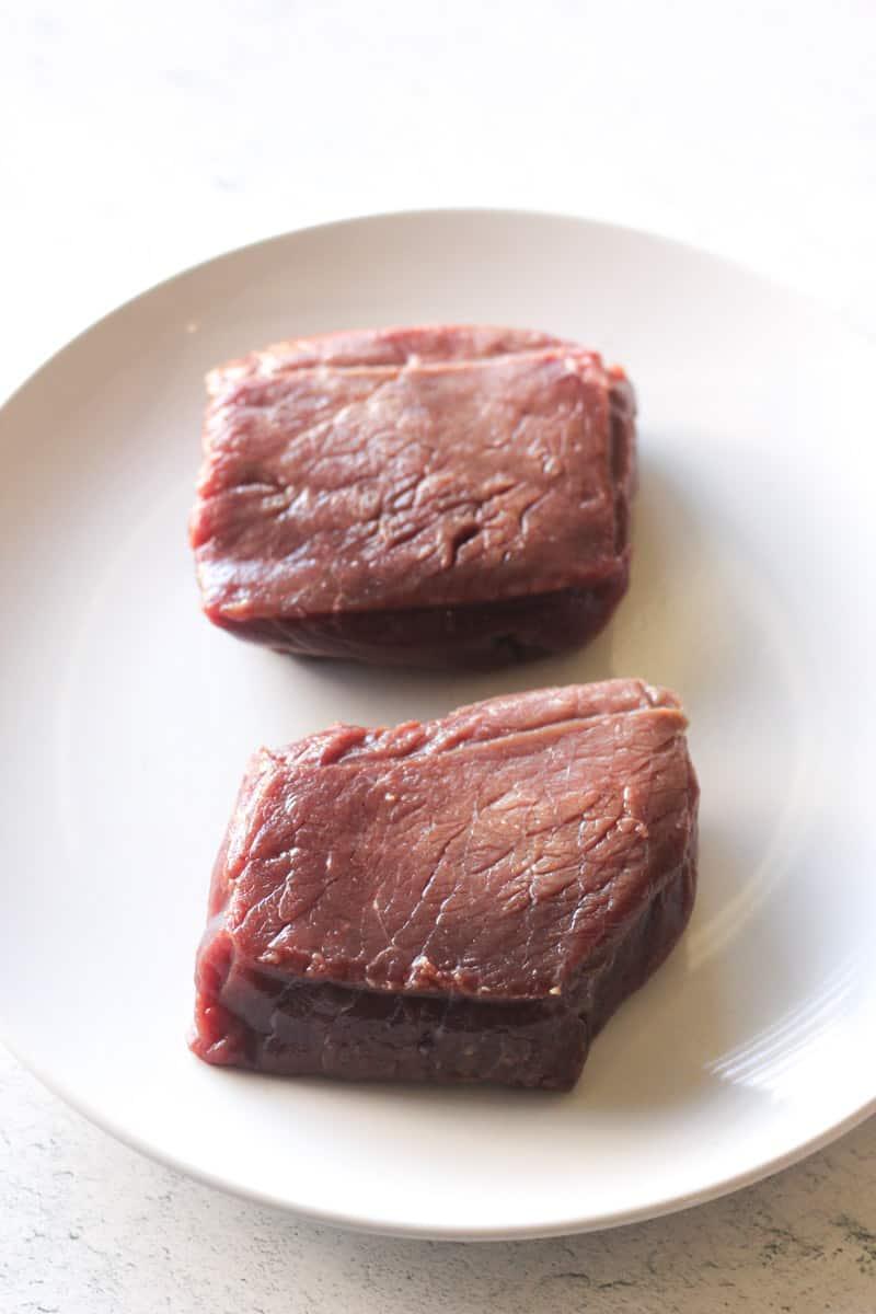 raw meat steaks on a white plate