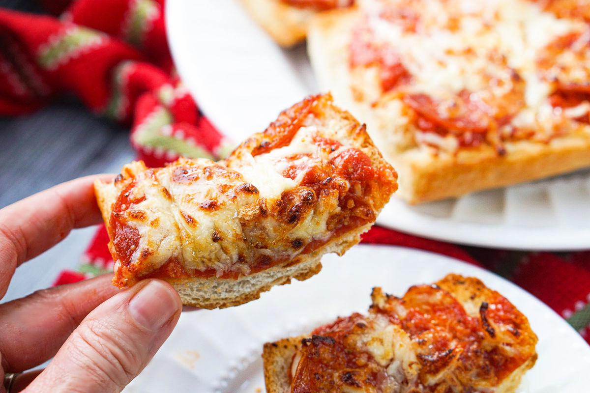 fingers holding a sliver of pepperoni French bread pizza