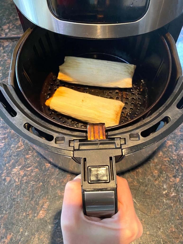 hand holding air fryer basket with two beef tamales inside