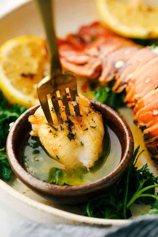 Lobster meat on a fork being dipped in a buttery herb garlic sauce.