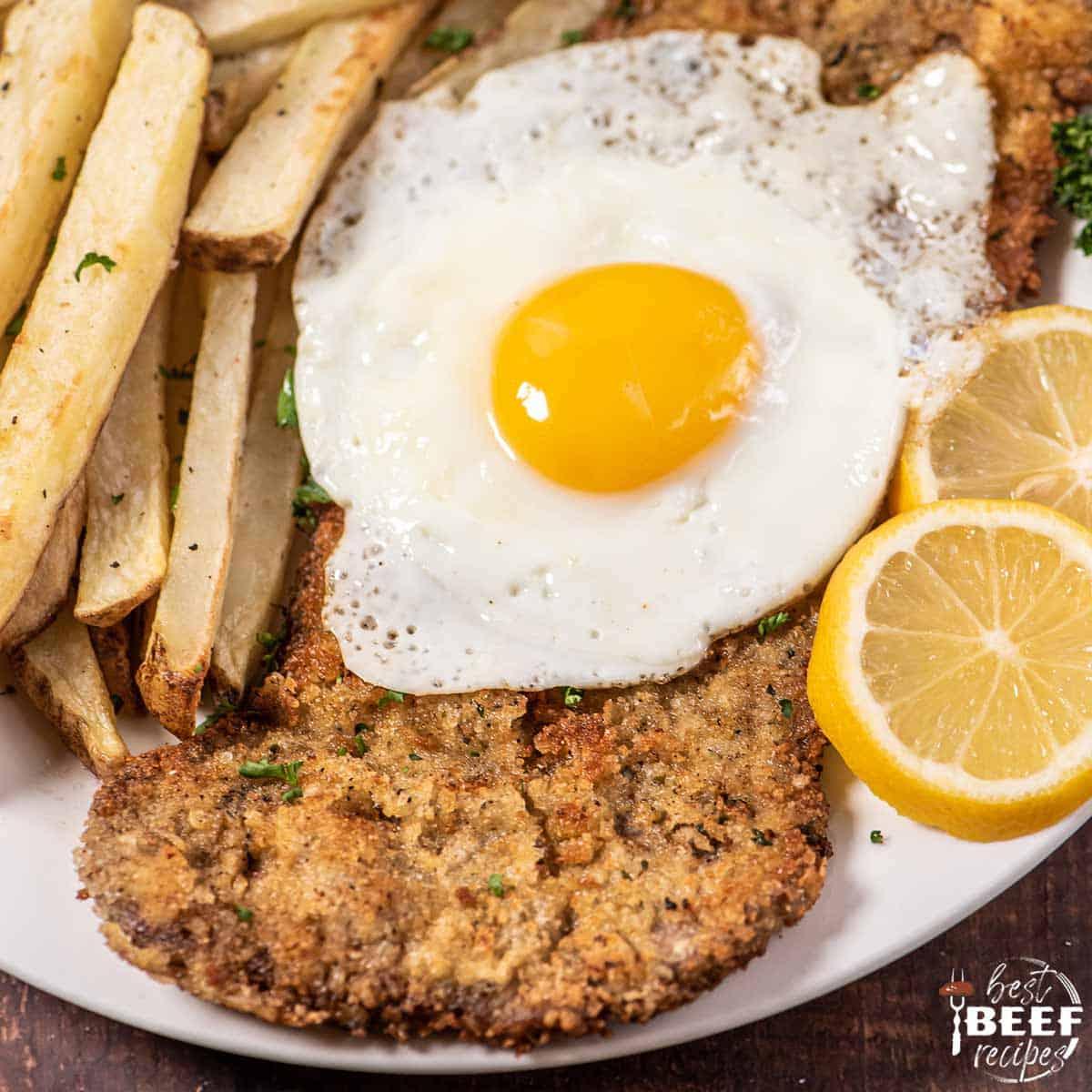 steak milanesa on a plate with an egg and fries