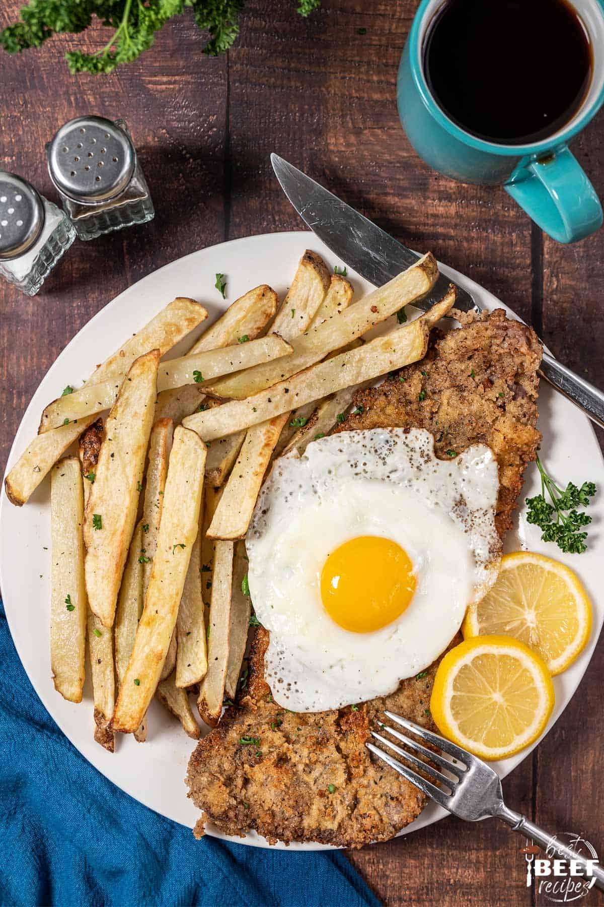 milanesa de res on a plate with fries, egg, and lemon slices