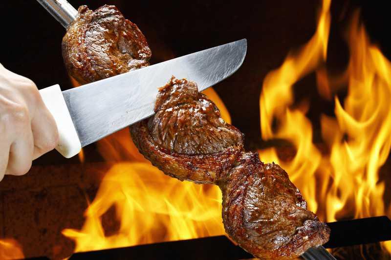 grilled rump cover or culotte steak in long metal skewer close to open flames