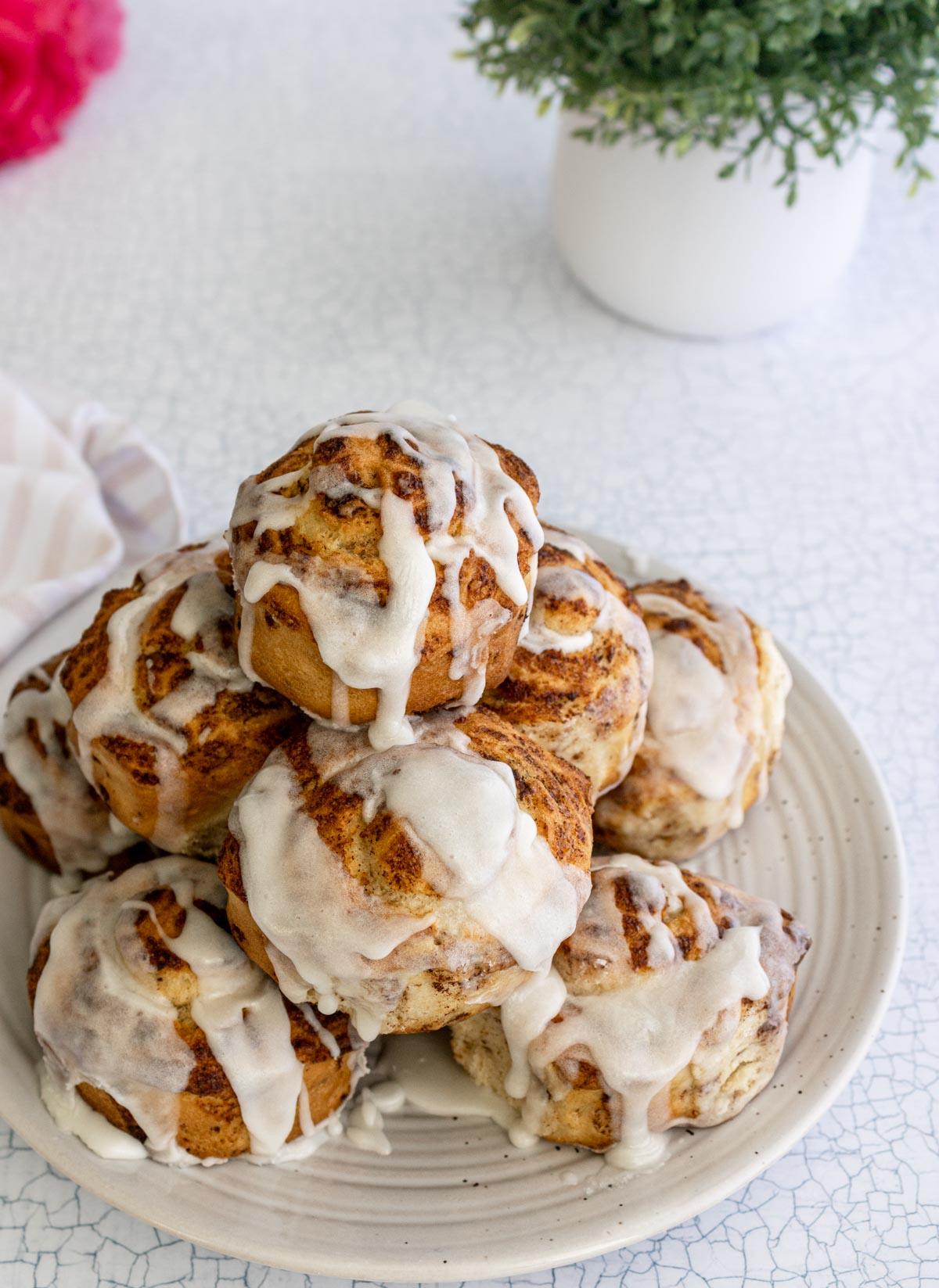 frosted air fryer cinnamon rolls stacked on a plate.