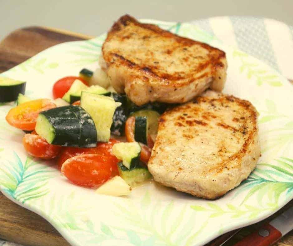grilled blackstone pork chops on a plate with veggies on the side