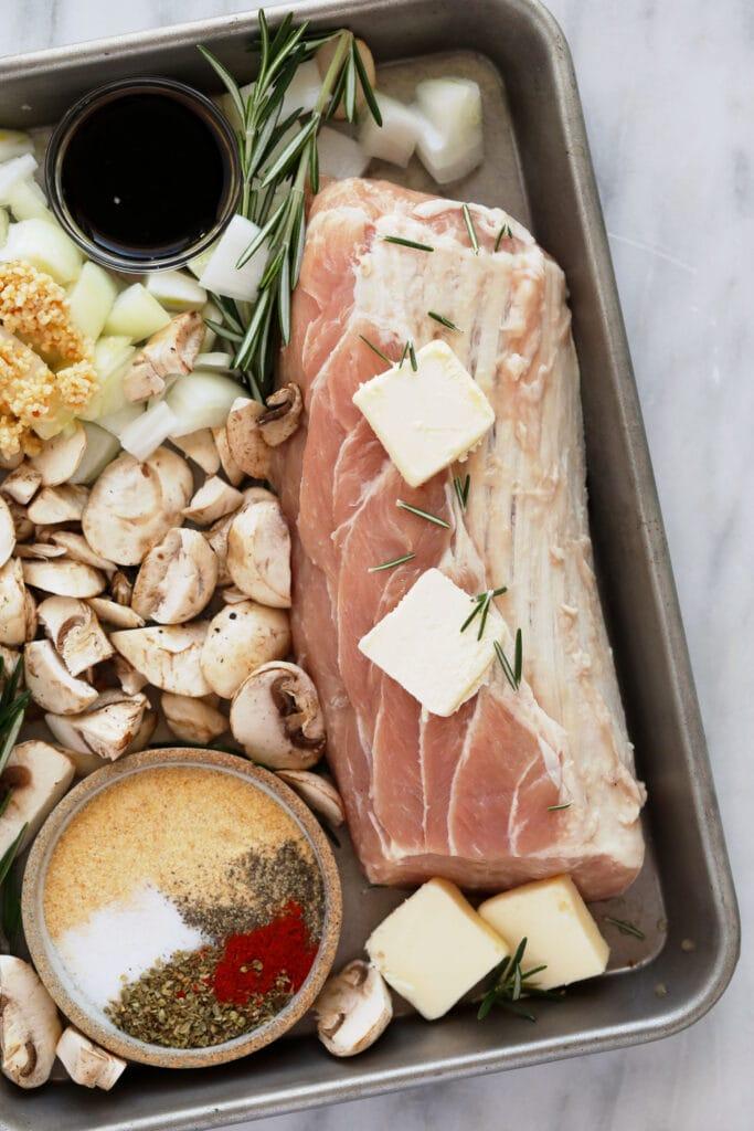 raw pork with mushrooms and butter on sheet pan.